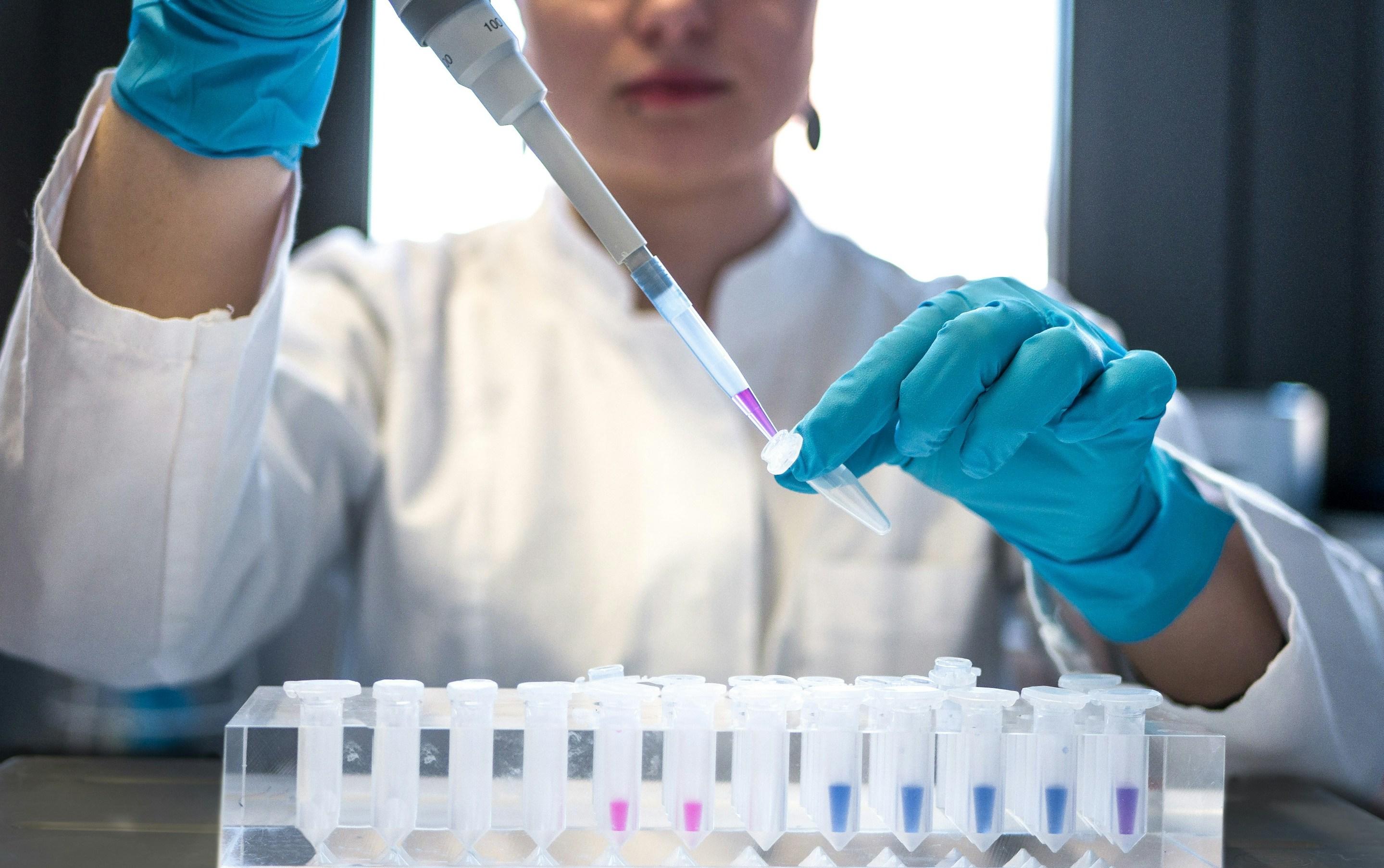 Gloved hand holding a pipette in the genomics lab